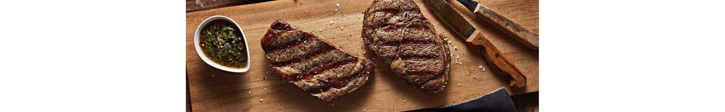 Steak resting on a cutting board next to a bowl of chimichurri sauce
