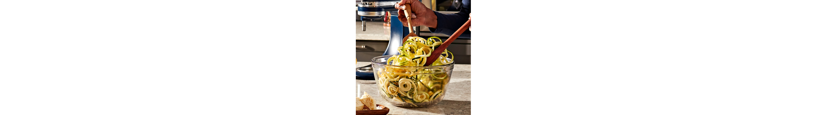 Woman tossing salad with veggie noodles in a glass salad bowl