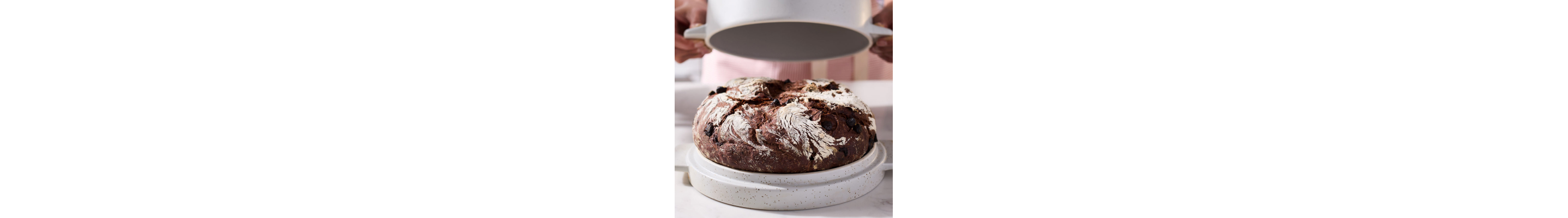 Maker uncovering top of bread bowl to reveal baked rye bread loaf