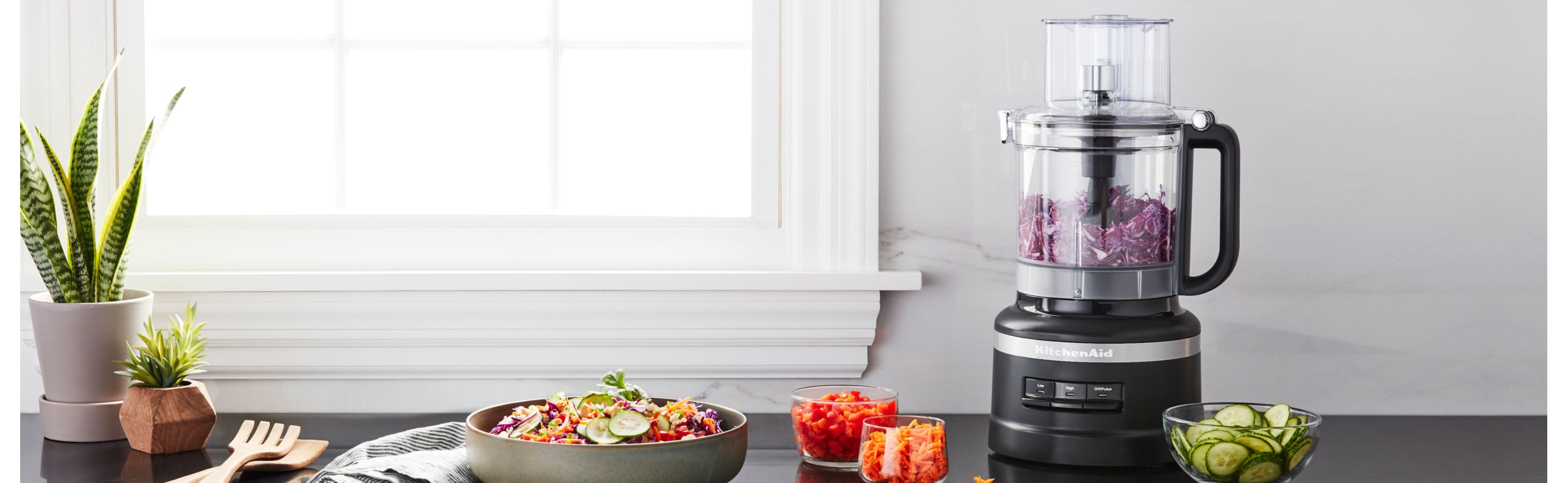 KitchenAid® food processor on a counter among chopped and sliced vegetables.