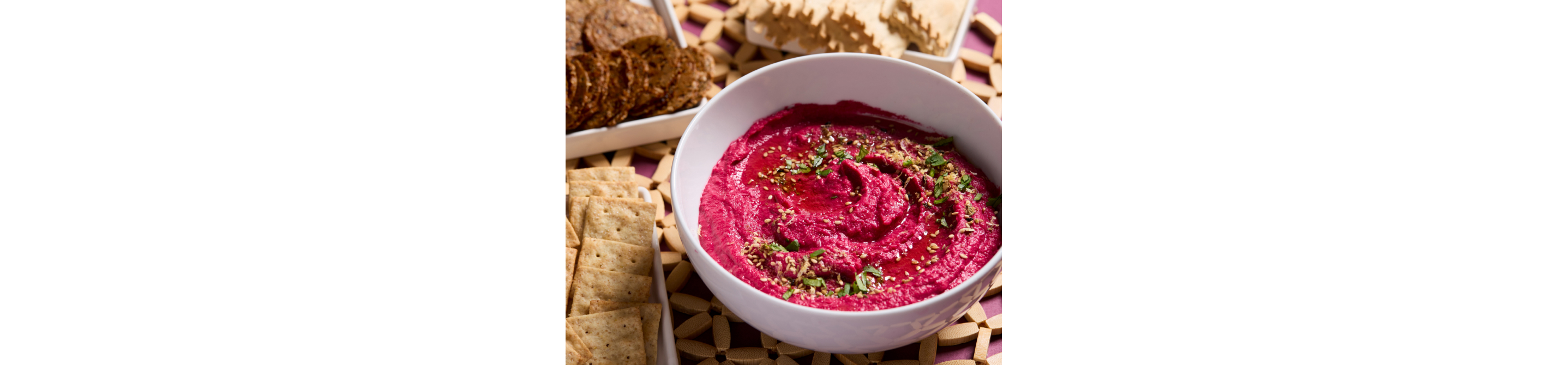 Beetroot hummus surrounded by an assortment of crackers
