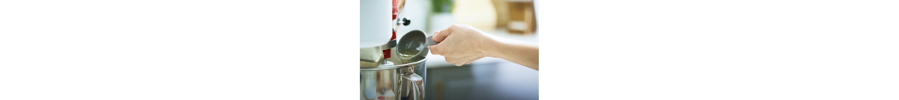 A person pouring oil into a KitchenAid® stand mixer bowl.
