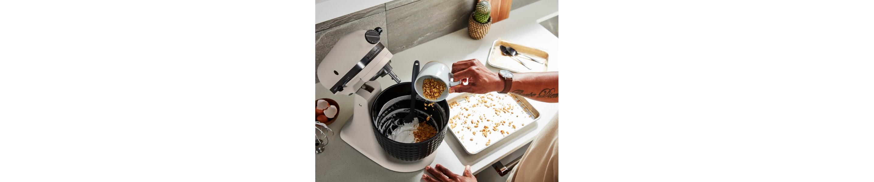 Person adding ingredients to black stand mixer bowl attached to white stand mixer