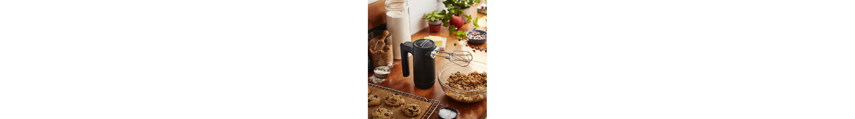 Black KitchenAid® hand mixer above bowl of cookie dough next to pan of baked cookies
