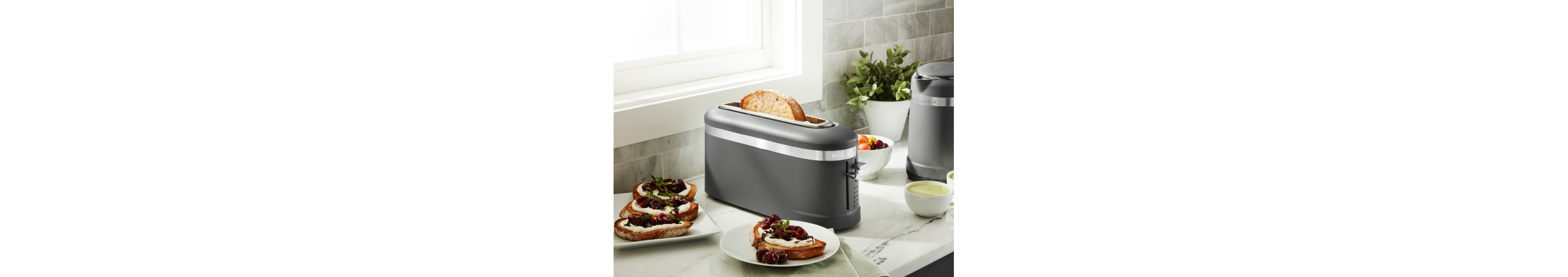 Toaster on a kitchen counter next to toast with fruit preserves 