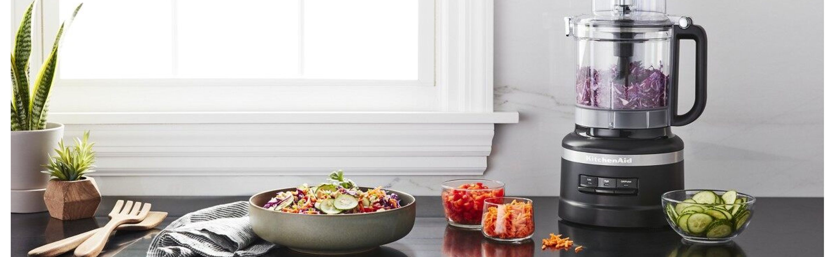 Black food processor on counter surrounded by processed vegetables and a bowl of salad