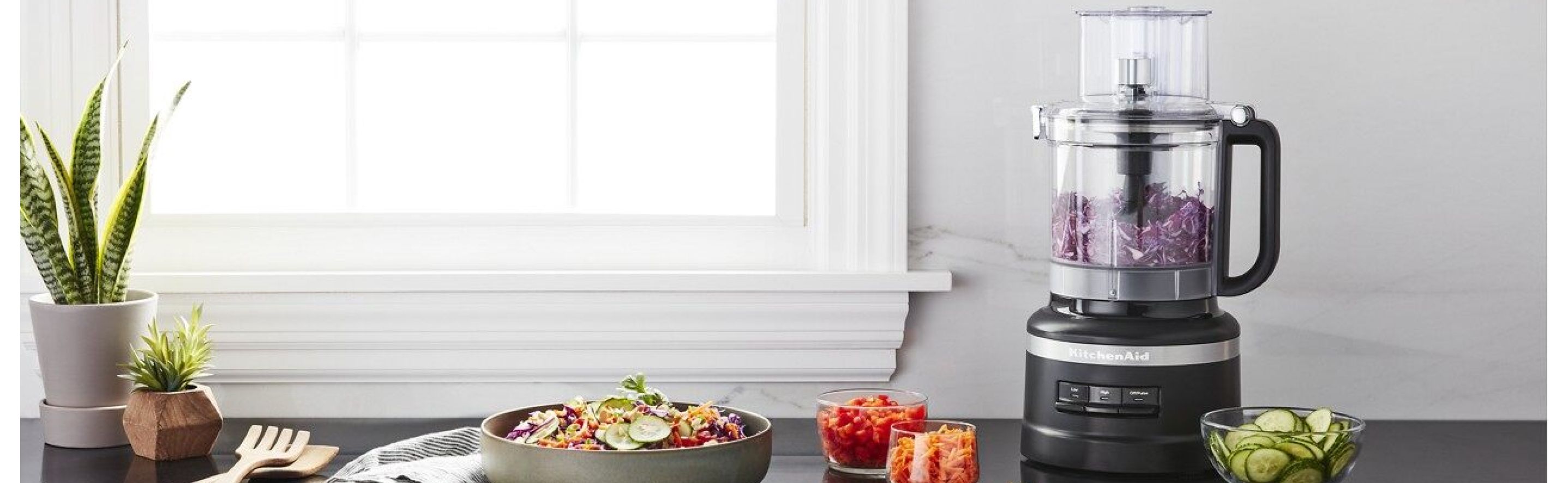 Black KitchenAid® food processor with shredded cabbage next to a salad