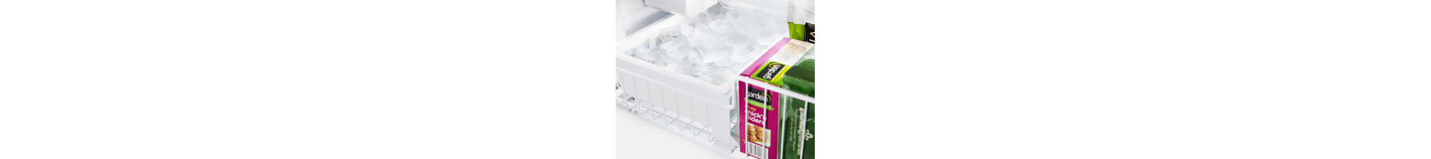 Full ice maker bin inside of a freezer next to frozen goods
