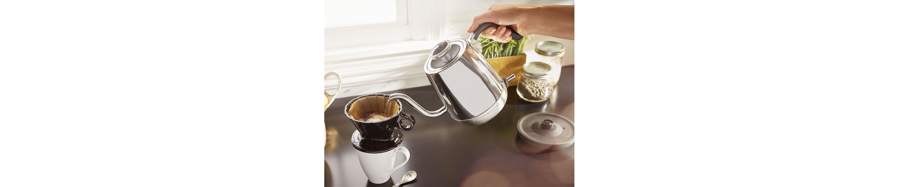 Person pouring hot water with silver KitchenAid® electric kettle