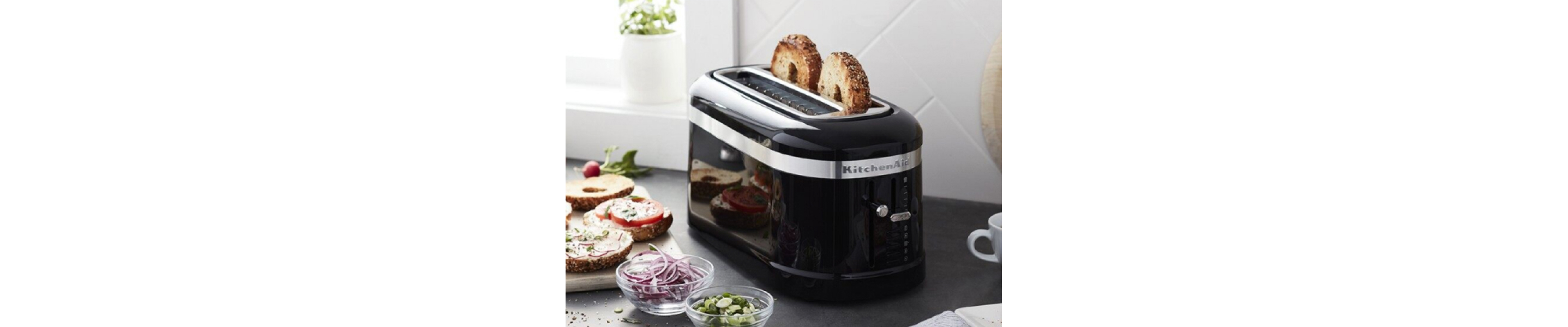 Black KitchenAid® toaster with two bagels inside sitting on counter with ingredients