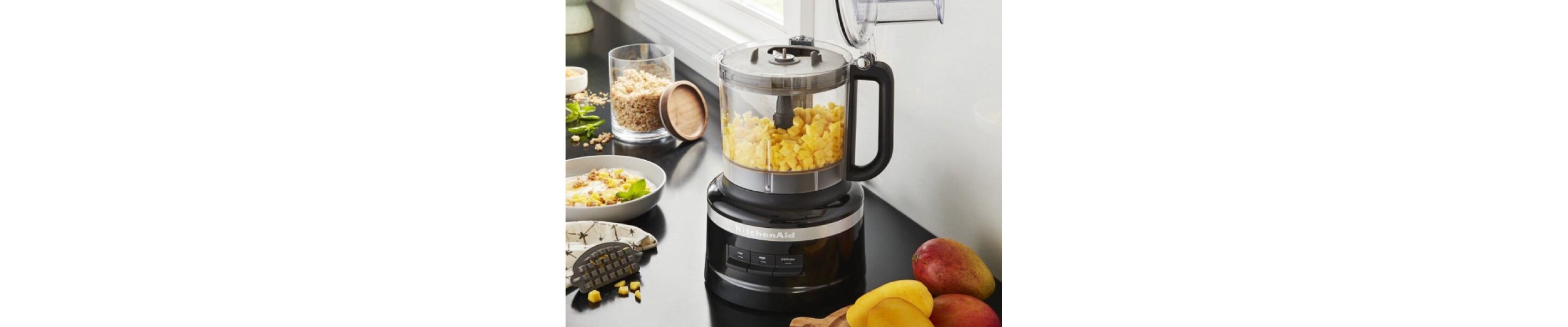 Black KitchenAid® food processor filled with corn kernels on counter with ingredients