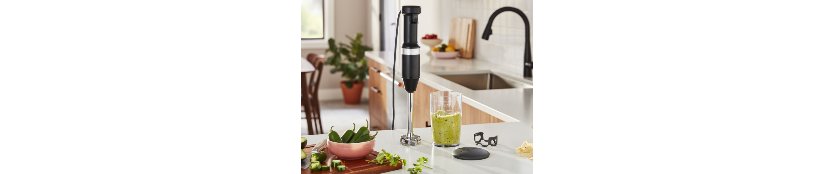 Black KitchenAid® hand blender on counter with blending cup and ingredients