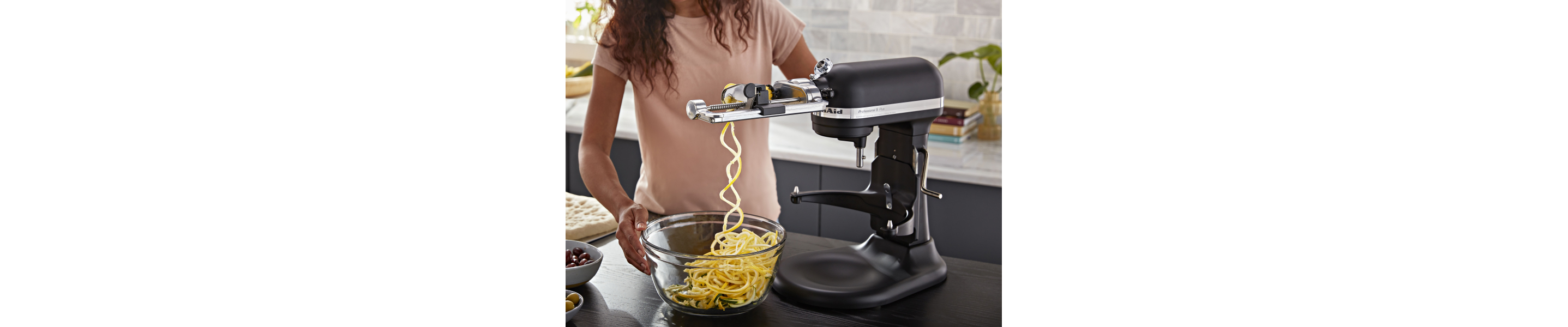 Matte black KitchenAid® stand mixer spiralizing food with the Spiralizer with Peel, Core and Slice Attachment