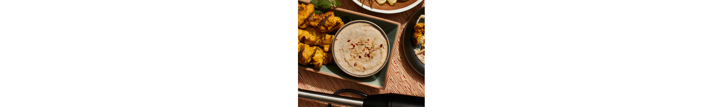 Immersion blender on table with satay chicken and sauce