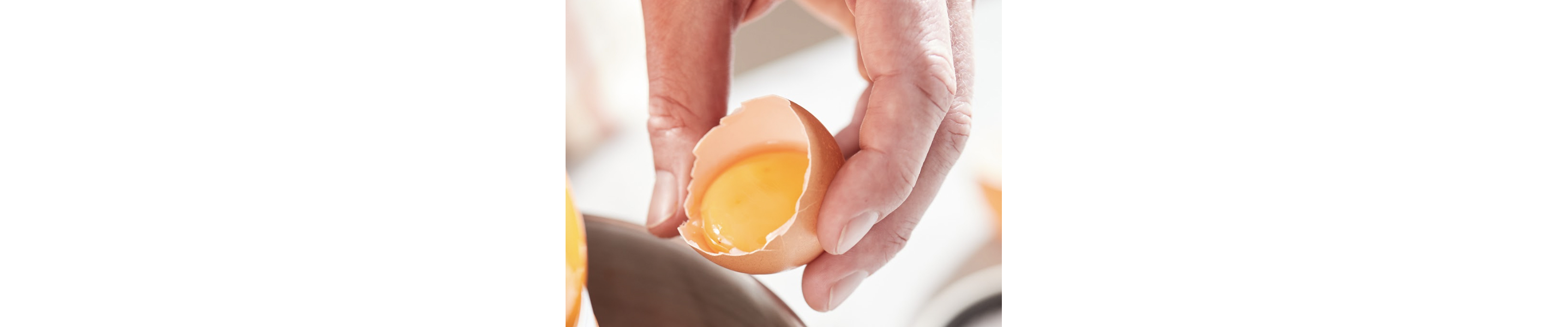A person holding a cracked egg shell with yolk inside