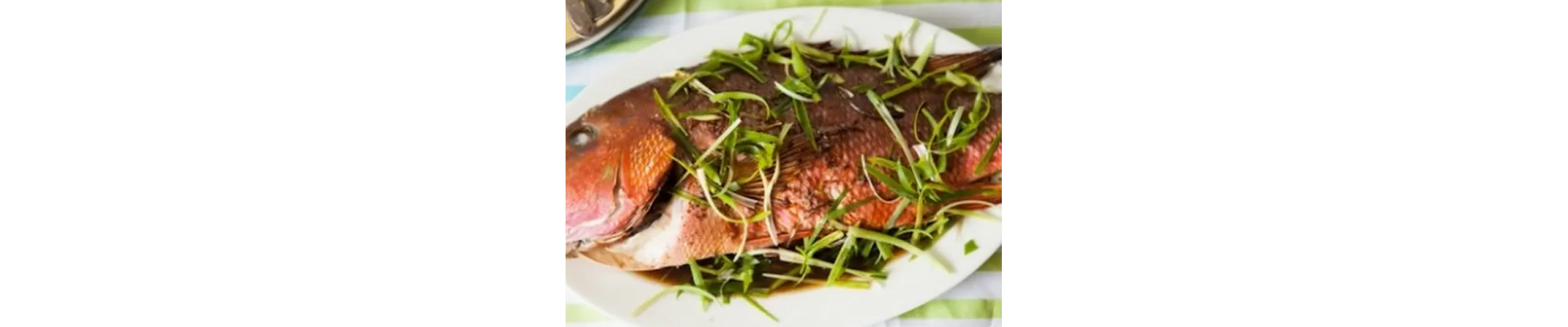 Roasted whole fish on white platter with fresh herbs