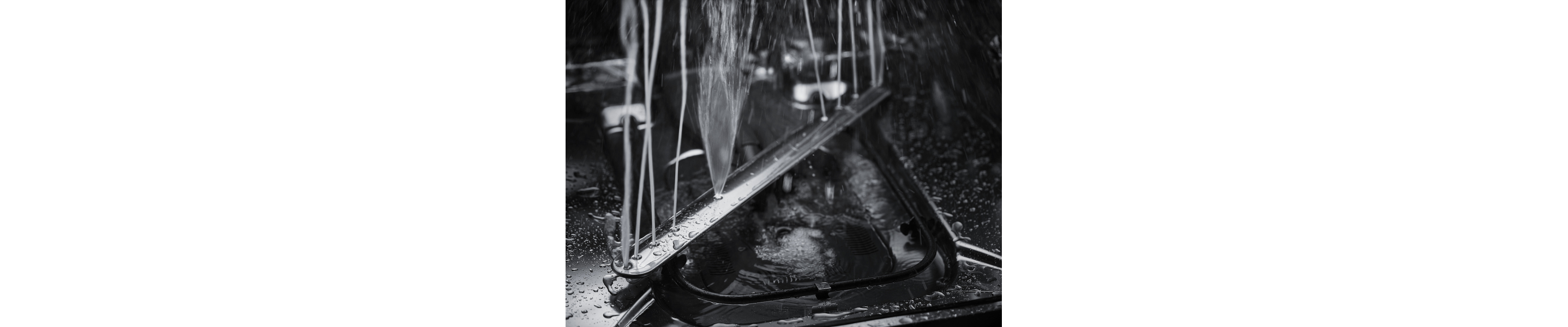 A closeup of a spray arm at the base of a KitchenAid® dishwasher spraying water.
