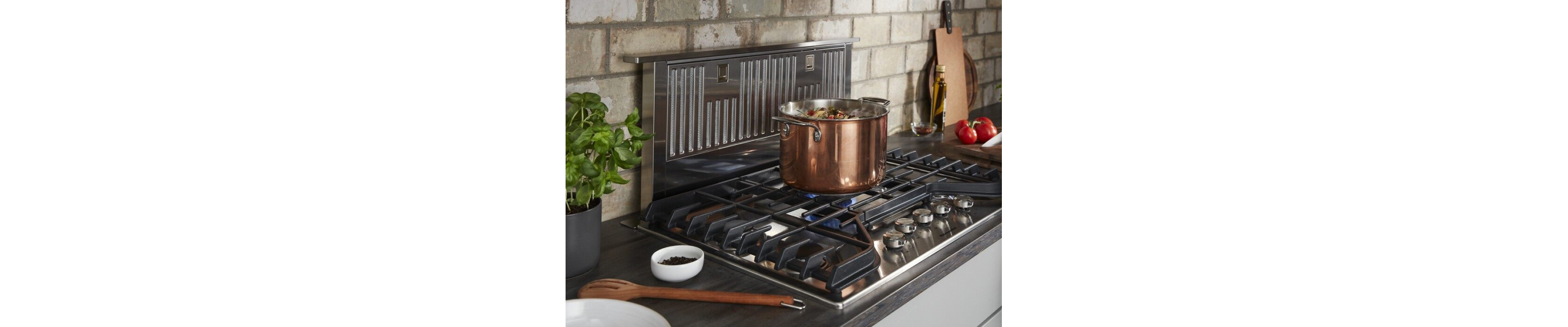 Stock pot on lit gas burner in front of a downdraft range hood