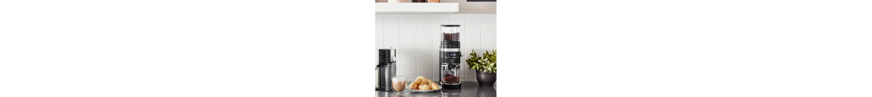 KitchenAid® burr coffee grinder next to a frothy cappuccino and pastries