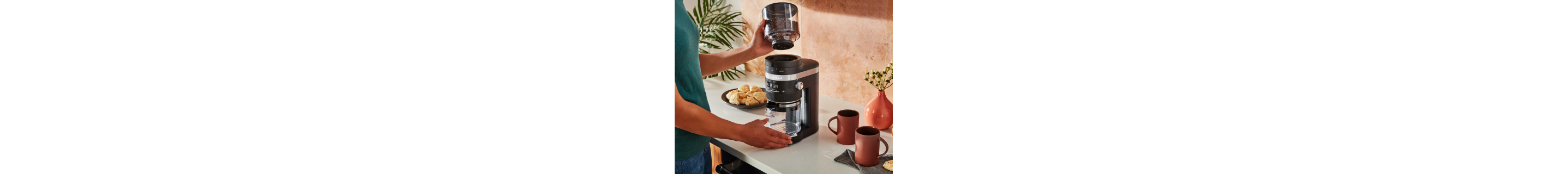 A woman using a KitchenAid® burr coffee grinder in a modern kitchen
