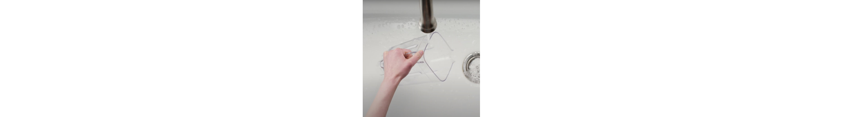 Hand holding KitchenAid® blender jar under the faucet over sink of soapy water