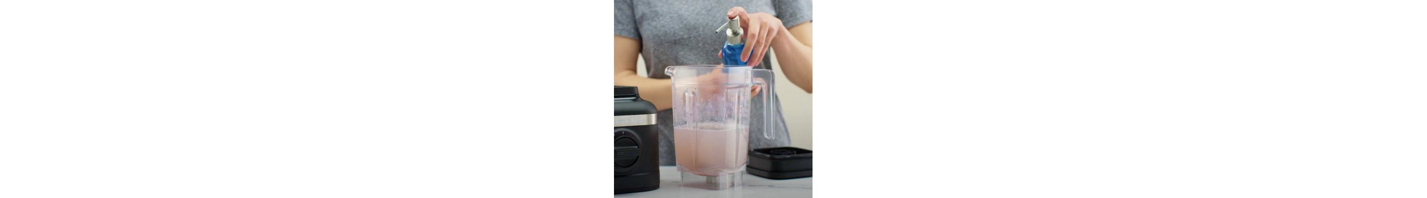 Person dispensing dish soap into KitchenAid® blender jar half-filled with water next to black base