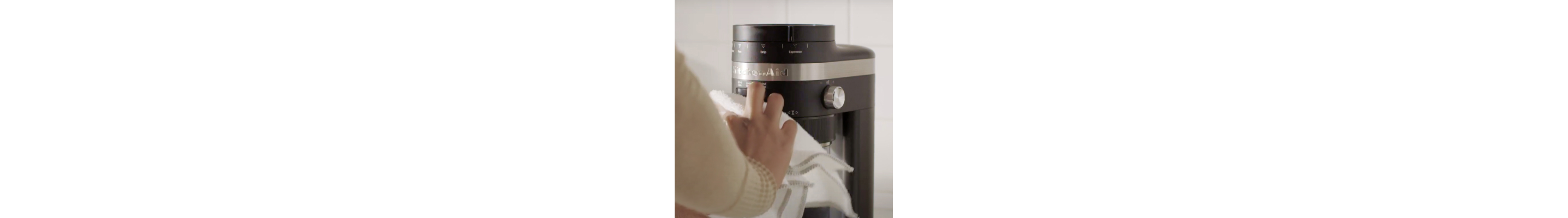 Hand wiping down the exterior of a KitchenAid® Burr Grinder with a towel