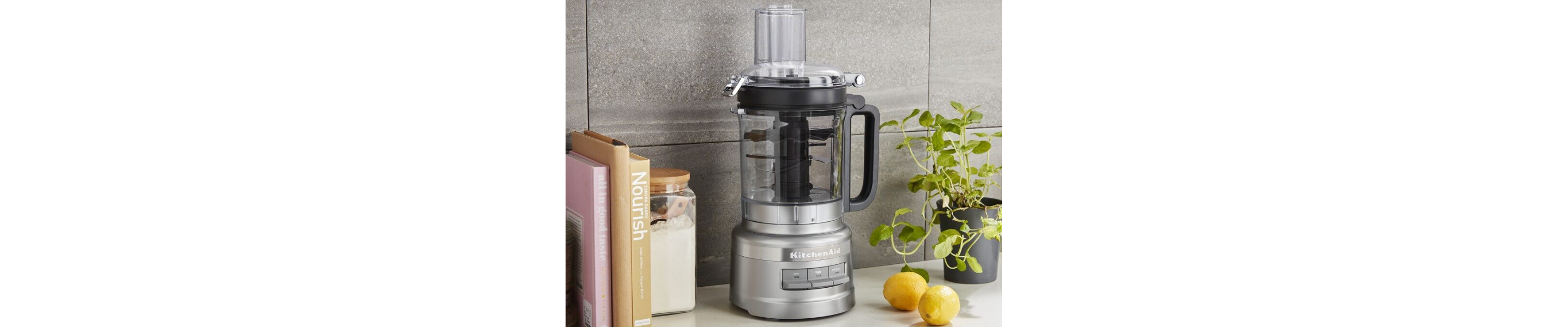 A KitchenAid® food processor sitting on a countertop next to various kitchen items