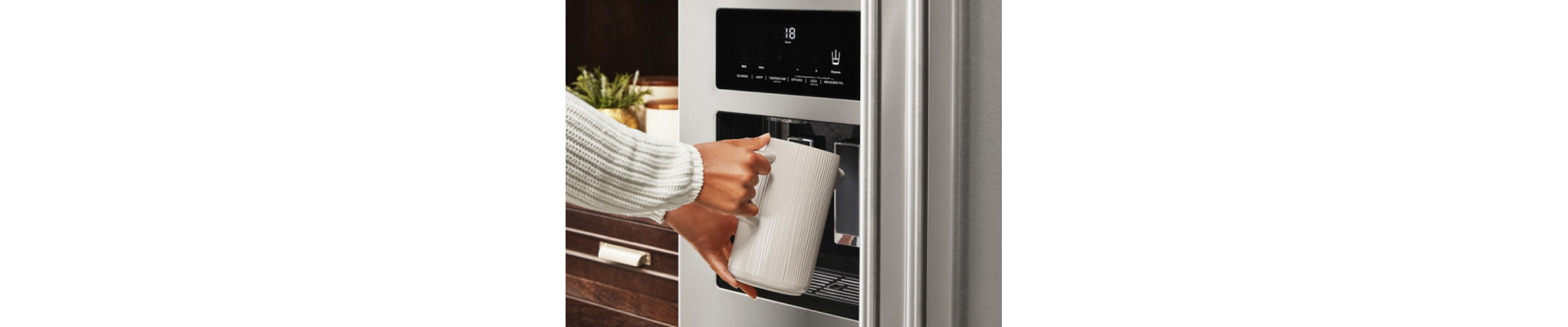 A woman filling a cup with water from a KitchenAid® refrigerator