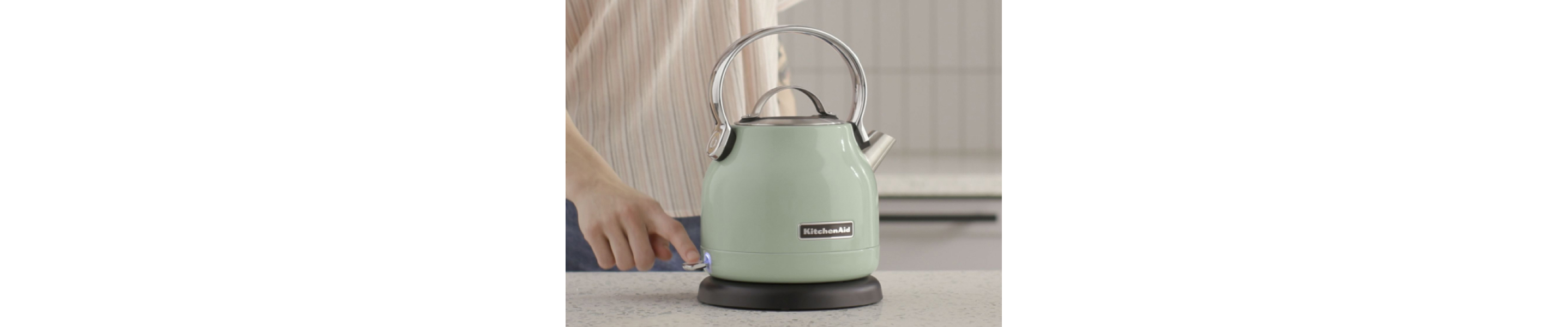 A woman using a KitchenAid® electric kettle in a modern kitchen