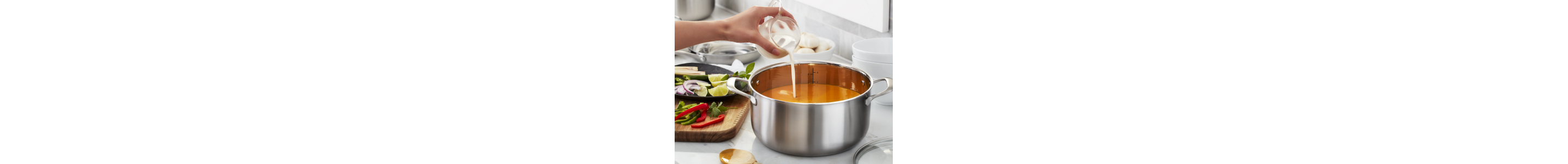 A closeup of a hand pouring milk into a pot of soup.