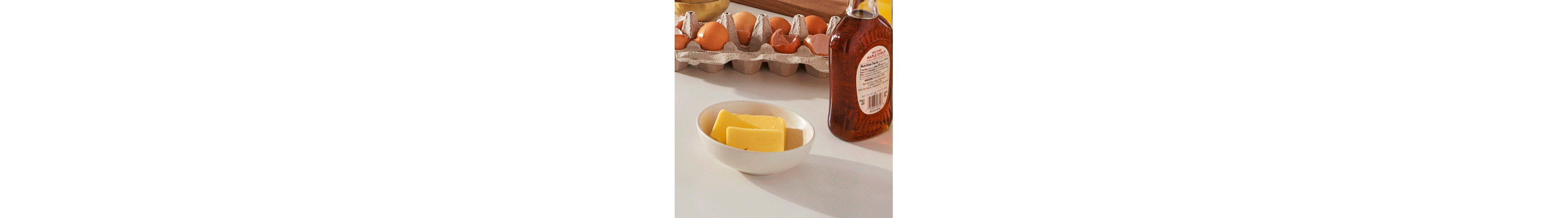 Butter, eggs and maple syrup on a white countertop