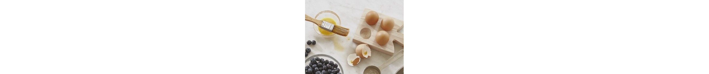 Ingredients including eggs next to egg wash and  beside a bowl of blueberries