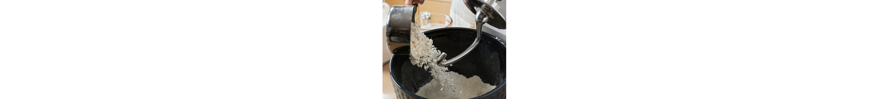 Flour pouring into a stand mixer bowl with a dough hook 
