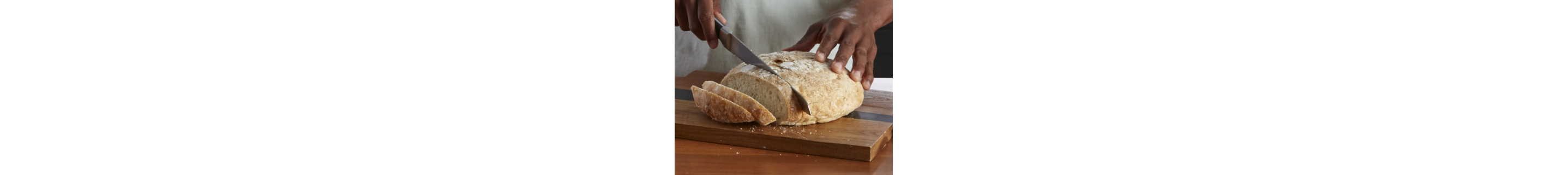 Person slicing a loaf of bread on a cutting board