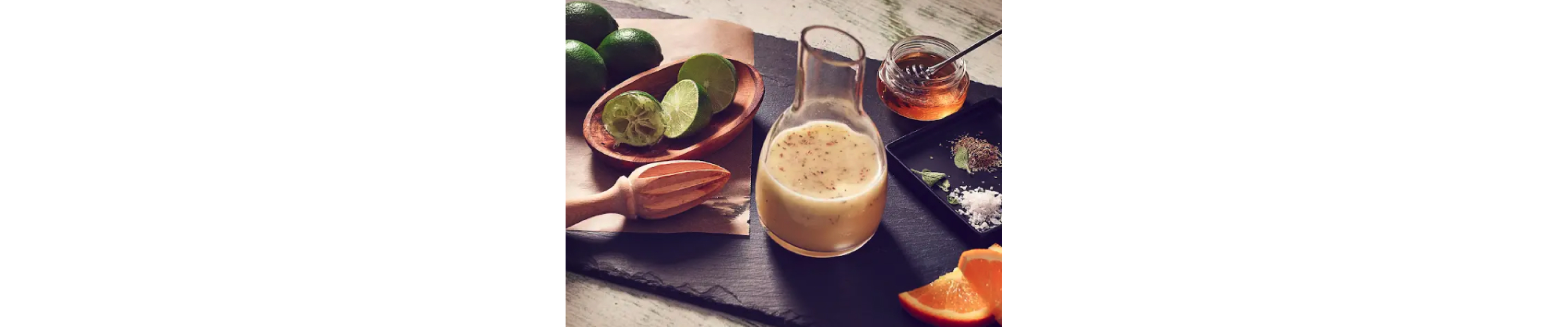 Homemade salad dressing in a glass serving jar next to limes and other ingredients.