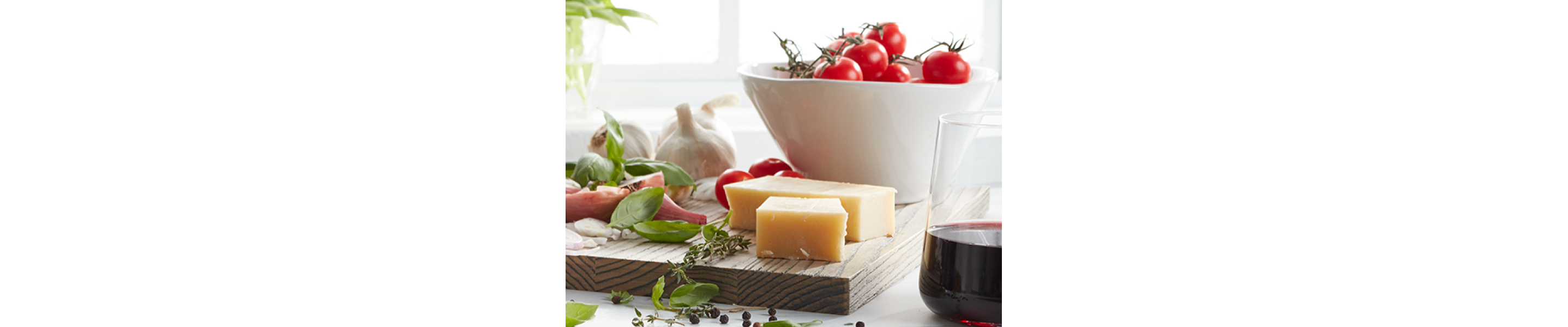 Wood block cutting board with cheese blocks and a bowl of vine tomatoes on top