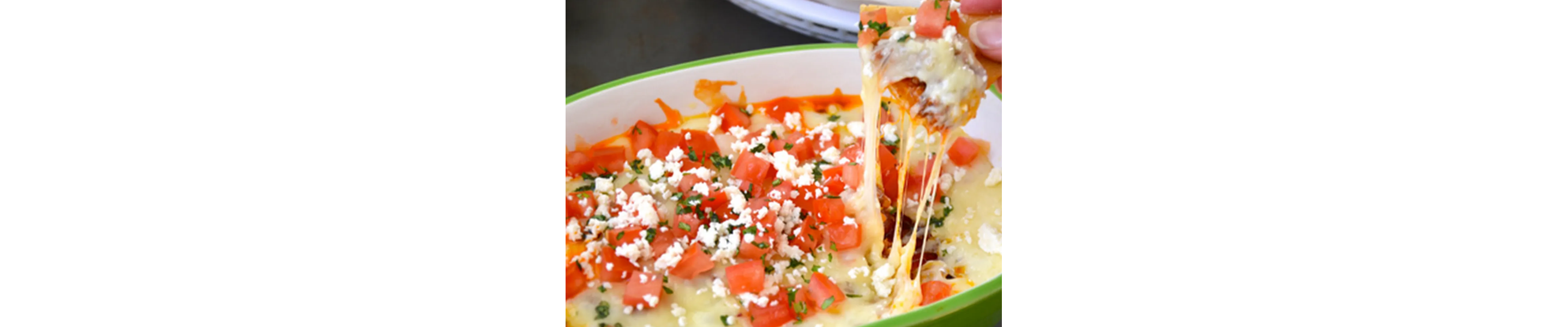 Person dipping chips into bowl homemade queso with fresh tomatoes on top