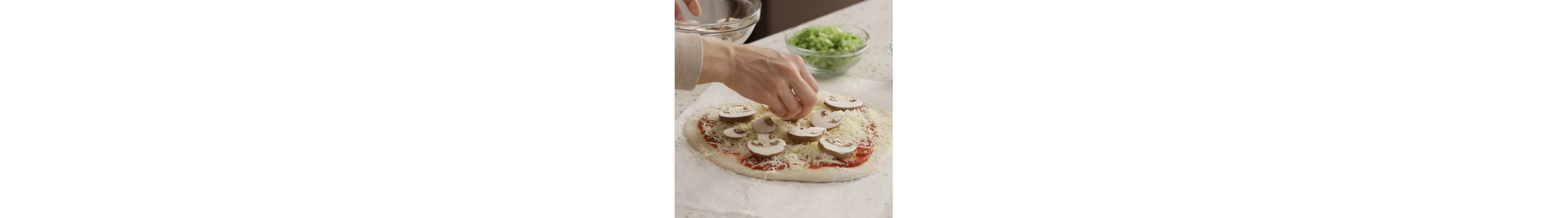 Person adding sliced mushrooms on top of a homemade pizza