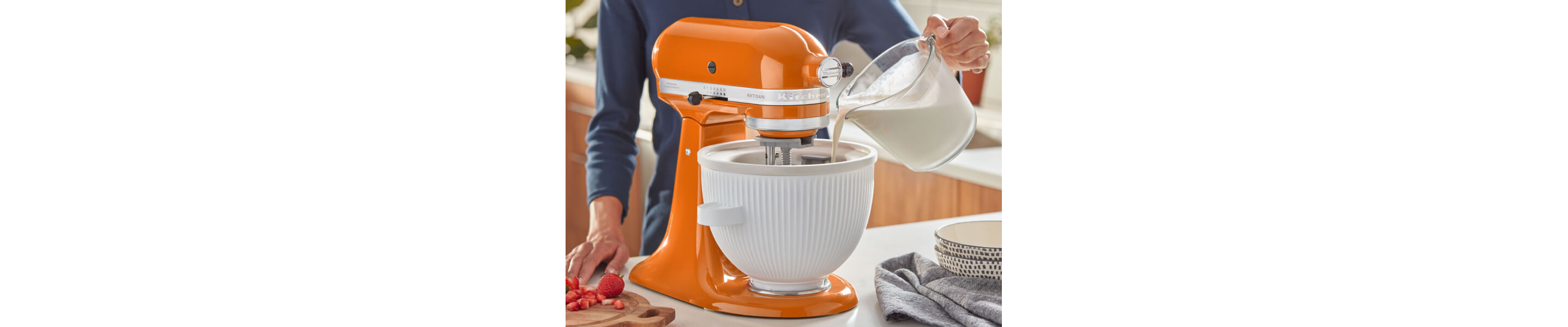 Hand pouring ice cream mixture into a KitchenAid® stand mixer bowl