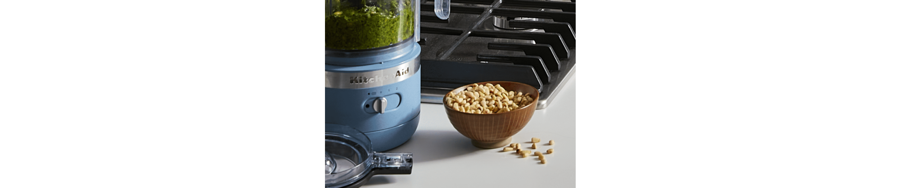A KitchenAid® food processor with a bowl of nuts nearby.