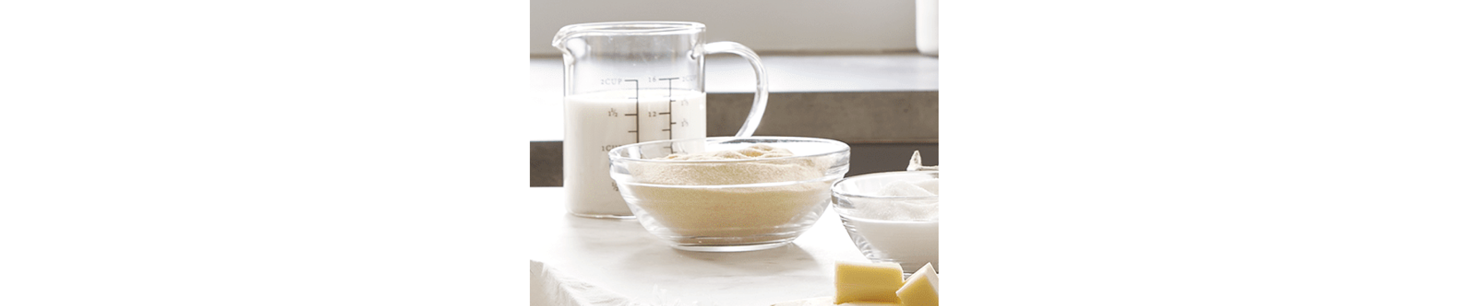 A measuring cup of milk and a bowl of yeast.