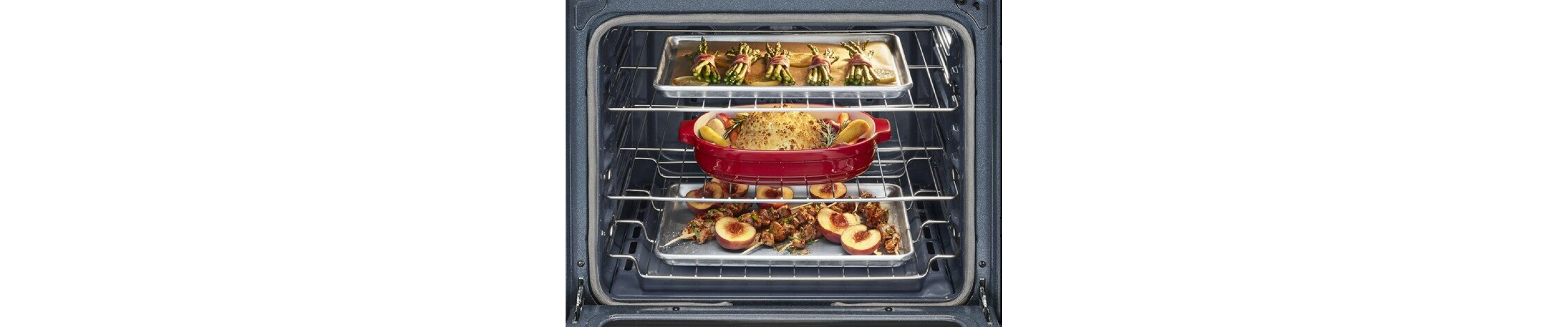 Open kitchen oven with roasting vegetables, fruits and meat on different racks