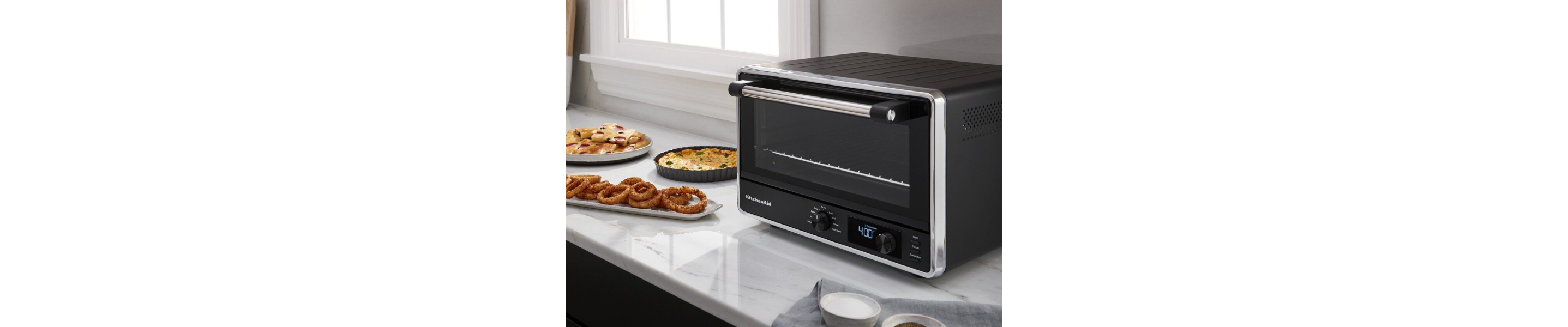 Black KitchenAid brand countertop oven on granite countertop next to finished dishes