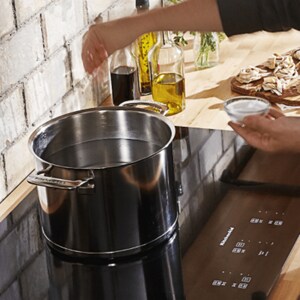 A person adding salt to water before boiling it