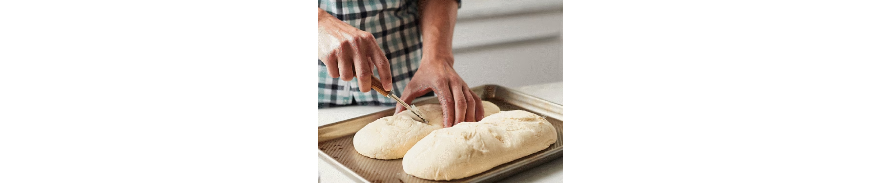 Person scoring two loaves of bread dough on a cookie sheet