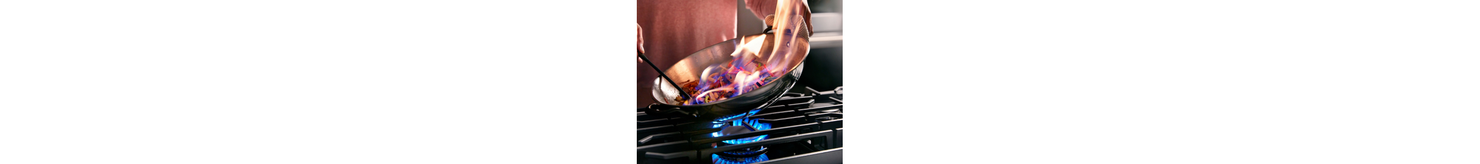 Hands cooking a flambe dish in a skillet over a gas stovetop