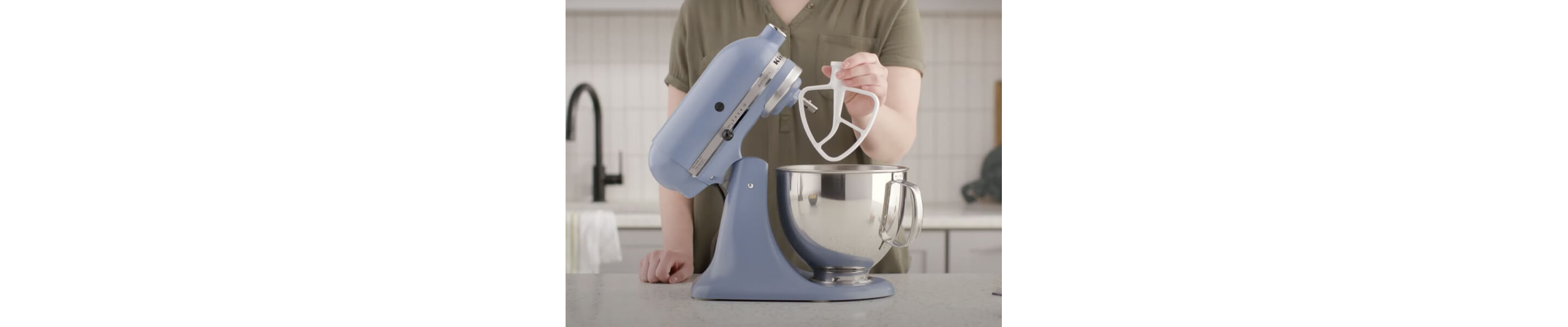 Woman holding a flat beater attachment next to a KitchenAid® stand mixer.