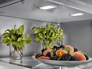 Herbs stored upright in glasses with water on the top shelf of a refrigerator
