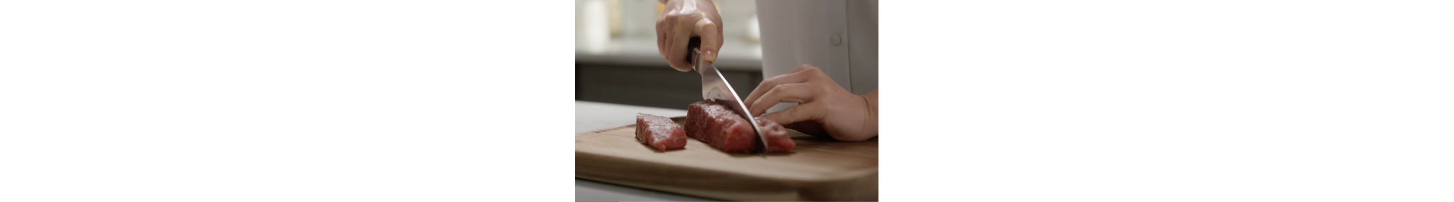 Person cutting meat with knife on a wood cutting board
